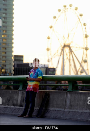 Young man holding mobile phone, skateboard beside him Stock Photo