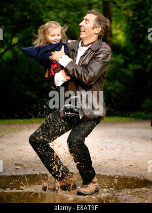 Father holding daughter, splashing in puddle Stock Photo
