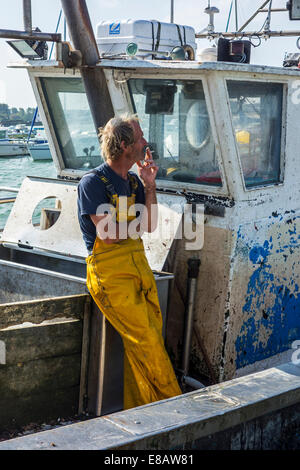 Fisherman smoking cigarette on board of trawler fishing boat docked in harbour Stock Photo
