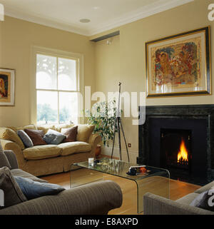 Large picture above fireplace with lighted fire in country living room with modern perspex table and beige sofa Stock Photo