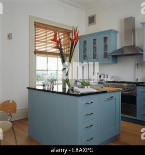 Birds-of-Paradise flowers in glass vase on pale blue granite-topped island unit in modern white kitchen with blue fitted units Stock Photo