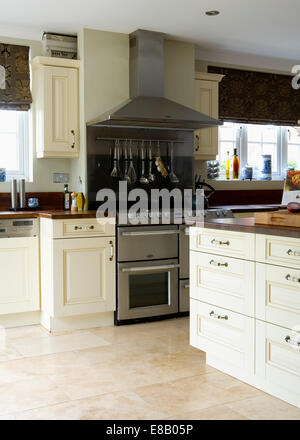 Cream travertine floor tiles in modern kitchen with large stainless steel range oven and cream fitted units Stock Photo