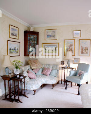 Pictures above pale blue Victorian corner sofa in country living sitting room with antique furniture and white carpet Stock Photo