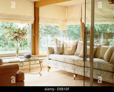 Glass doors open to modern conservatory living room extension with cream blinds and traditional neutral sofa Stock Photo