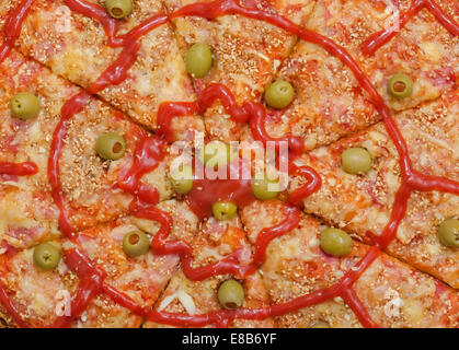 Background of Sliced Pizza with Ham, Bacon, Cheese, Green Olives filled with Paprika, Sesame , Garlic and Tomato Sauce, Closeup Stock Photo