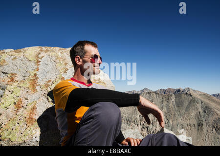 middle aged man sitting on a mountain top leaning against a rock Stock Photo
