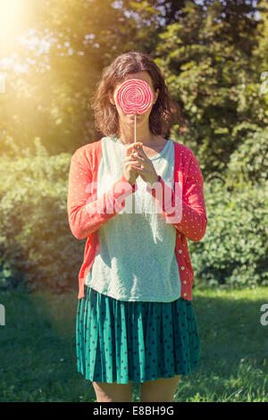 Cute hipster girl hiding her face behind a big lollipop Stock Photo