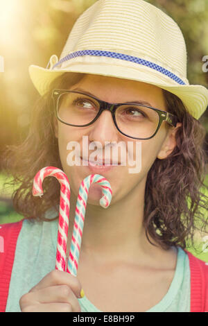 Happy Hipster teenage Girl Thinking of Sweets and holding Candy Canes. outdoor shot, retro colors Stock Photo