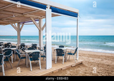 Sea side bar interior with wooden floor and metal armchairs on the sandy beach Stock Photo