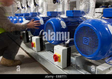 Row of Grouped water and refrigeration pumps, pump technology, power industry, air, electric controls, vented motors being attended to by engineer. Stock Photo