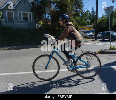 woman cycling with white cockatoo or parrot on handlebars of bicycle, Seattle, USA Stock Photo