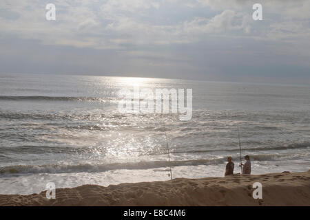 Two fishermen companionable fish together in the ocean on a beach in Cape Hatteras, NC near sunset Stock Photo