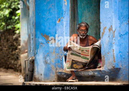 Indian man sitting on his doorstep reading a local newspaper Stock Photo