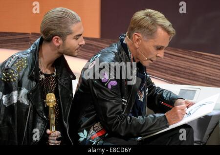 Erfurt, Germany. 5th Oct, 2014. German fashion designer Wolfgang Joop (R) draws as Tokio Hotel singer Bill Kaulitz looks over his shoulder during the ZDF show 'Wetten, dass.?' in Erfurt (Thuringia), Germany, 04 October 2014. Credit:  dpa picture alliance/Alamy Live News Stock Photo