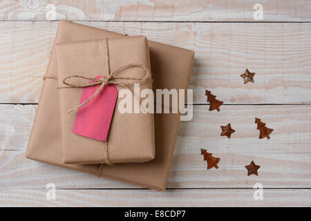 A high angle view of plain brown paper wrapped presents with red tags on a white rustic table. Small rusty metal ornaments in st Stock Photo