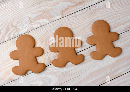 HIgh angle view of three gingerbread men on a rustic white kitchen table. The cookies are  plain and without icing. Stock Photo
