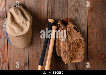 Vintage baseball equipment still life. A glove, two bats and hats against a rustic wooden wall. Horizontal format. Stock Photo