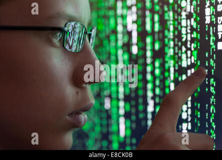 A young man with glasses is watching futuristic symbols on a computer screen. Symbols are reflecting in the man's glasses. Stock Photo