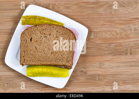 Closeup horizontal top view of Ham Sandwich made of whole wheat bread and pickles on the side with white plate and wooden board Stock Photo