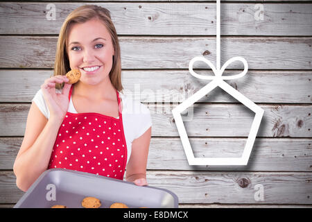 Composite image of pretty homemaker showing hot cookies Stock Photo