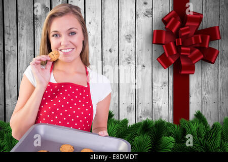 Composite image of pretty homemaker showing hot cookies Stock Photo