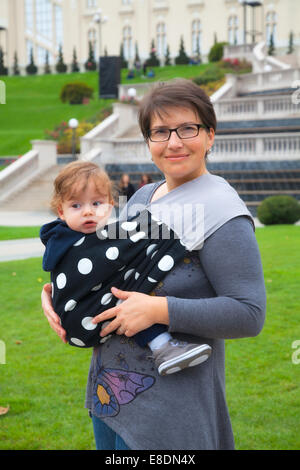 Portrait of mother wearing her baby boy in a sling in the park. Stock Photo