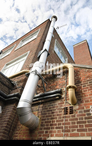 metal flue and chimney with steel heating pipes on outside of brick building tower no an energy efficient system Stock Photo