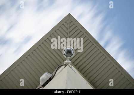 surveillance with remote controlled camera on face of corner of building architecture with reflective sky in window moving cloud Stock Photo