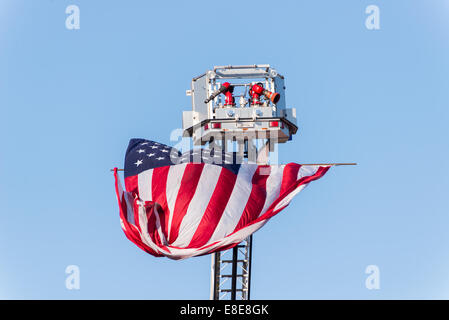 An American Flag is flying from an extended fire department ladder / aerial on a clear blue sky day Stock Photo