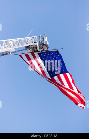 An American Flag is flying from an extended fire department ladder / aerial on a clear blue sky day Stock Photo