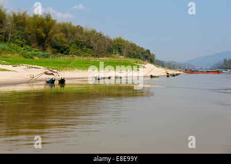 Horizontal view of traditional wooden fishing boats and passenger ferries moored up alongside the Mekong river in the dry season Stock Photo