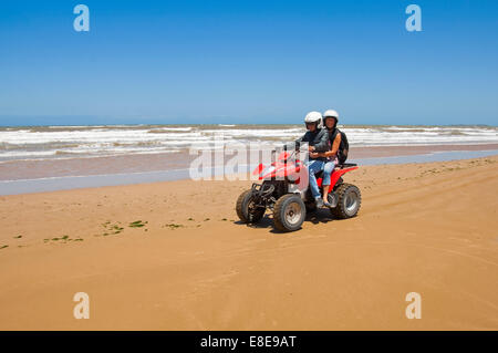 Horizontal portrait of a young man and woman on a quad bike on the beach on Morocco. Stock Photo