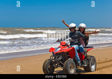 Horizontal portrait of a young man and woman on a quad bike on the beach on Morocco. Stock Photo