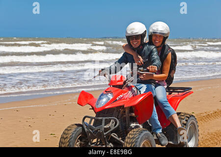 Horizontal portrait of a young man and woman on a quad bike on the beach on Morocco. Stock Photo