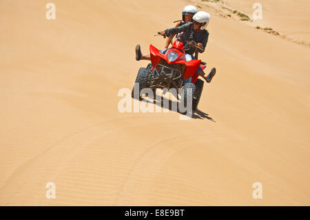 Horizontal portrait of a young man and woman on a quad bike on the beach on Morocco. Stock Photo