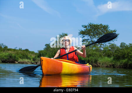 Young Woman Kayaking Alone on a Calm River and Wearing a Safety Vest Stock Photo
