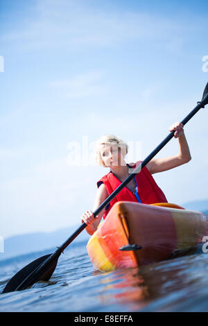 Young Woman Kayaking Alone on a Calm Sea and Wearing a Safety Vest Stock Photo