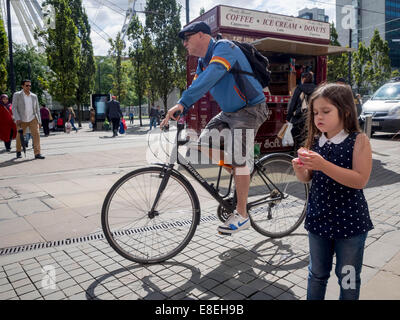 A Cyclist on the pavement cycles past a young girl in Manchester city centre Stock Photo