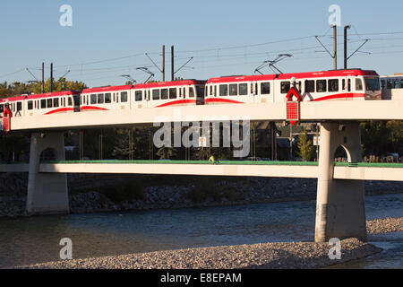 Light rail electric train powered by wind energy crossing Bow River and cyclist crossing on lower  pedestrian deck. Stock Photo