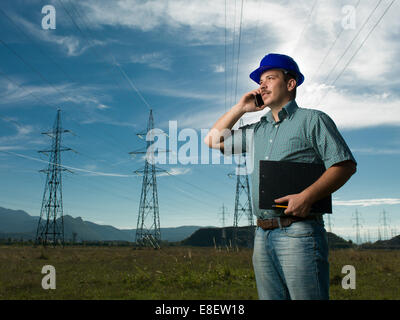 engineer standing on field with electricity towers, talking on the phone Stock Photo