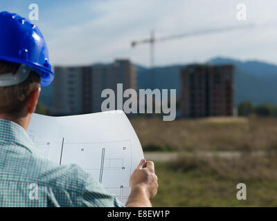 back view, closeup of male caucasian engineer at work looking at technical drawing plan Stock Photo