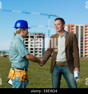 architect and construction engineer standing and shaking hands on construction site outdoors Stock Photo