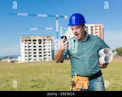 portrait of angry engineer standing on construction site, yelling at his phone Stock Photo