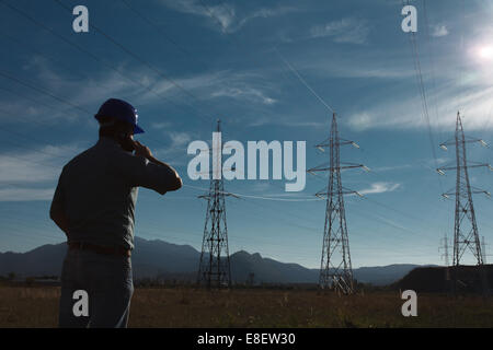silhouette of engineer standing on field with electricity towers, talking on the phone Stock Photo