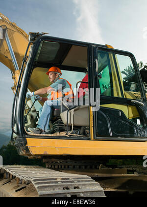 A construction worker operating a backhoe at a building site turns to ...