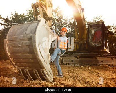 male engineer standing next to excavator on construction site outdoors, with sunlight in background Stock Photo