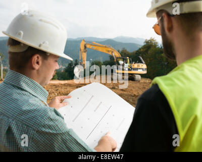 back view of two contractors looking at construction plan on worksite Stock Photo