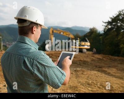 back view of caucasian engineer standing on construction site checking plan on digital tablet Stock Photo