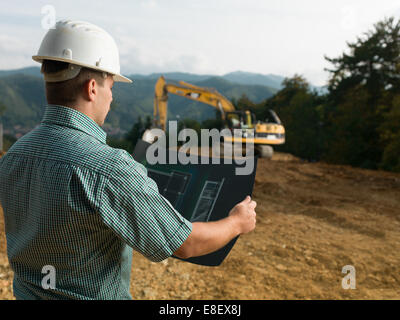 back view of male engineer standing on construction site reading blueprint Stock Photo