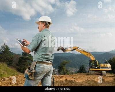back view of caucasian engineer standing on construction site browsing on digital tablet Stock Photo
